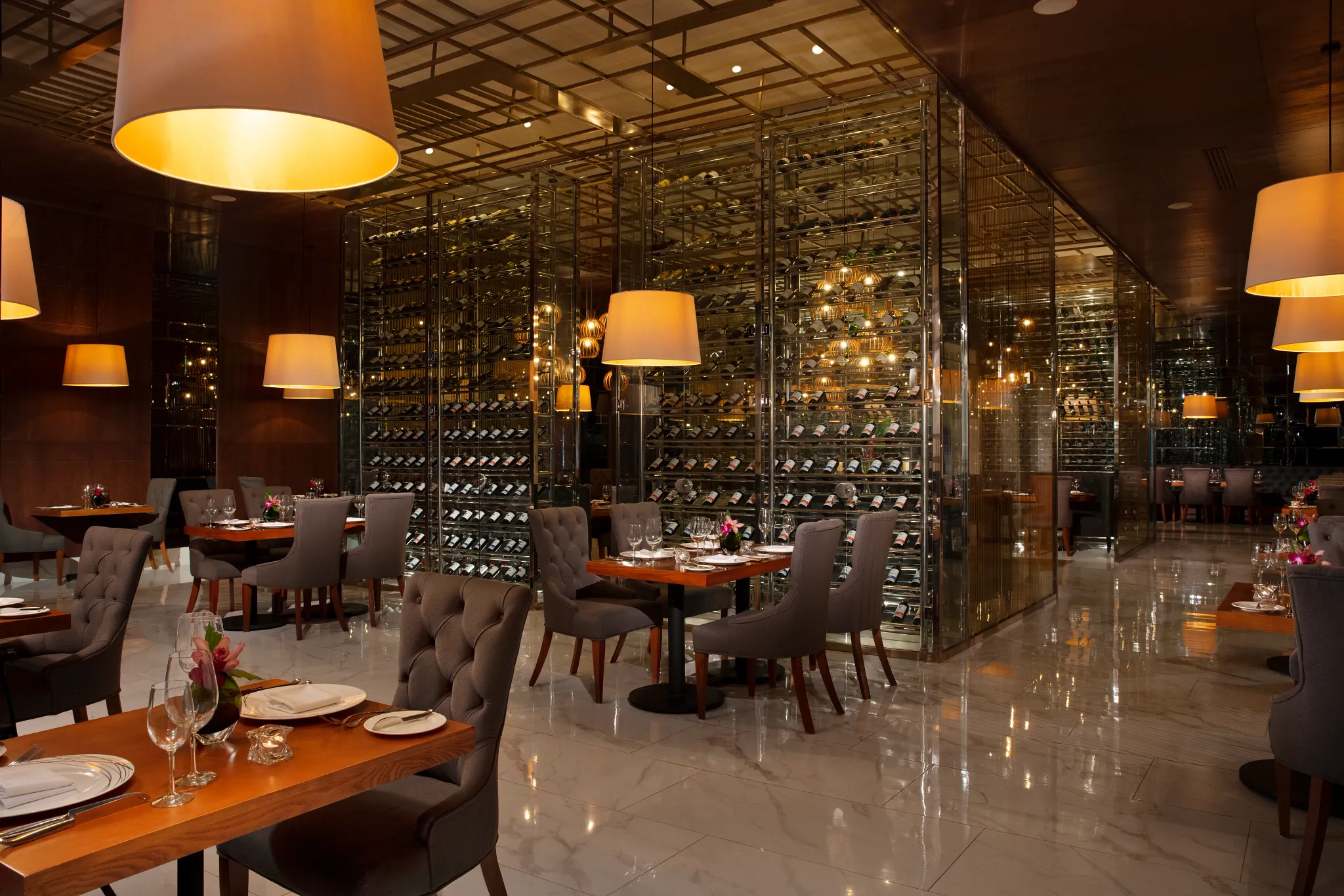 Bordeaux French Restaurant at Secrets Royal Beach Punta Cana featuring elegant dining tables and a glass-enclosed wine cellar display.