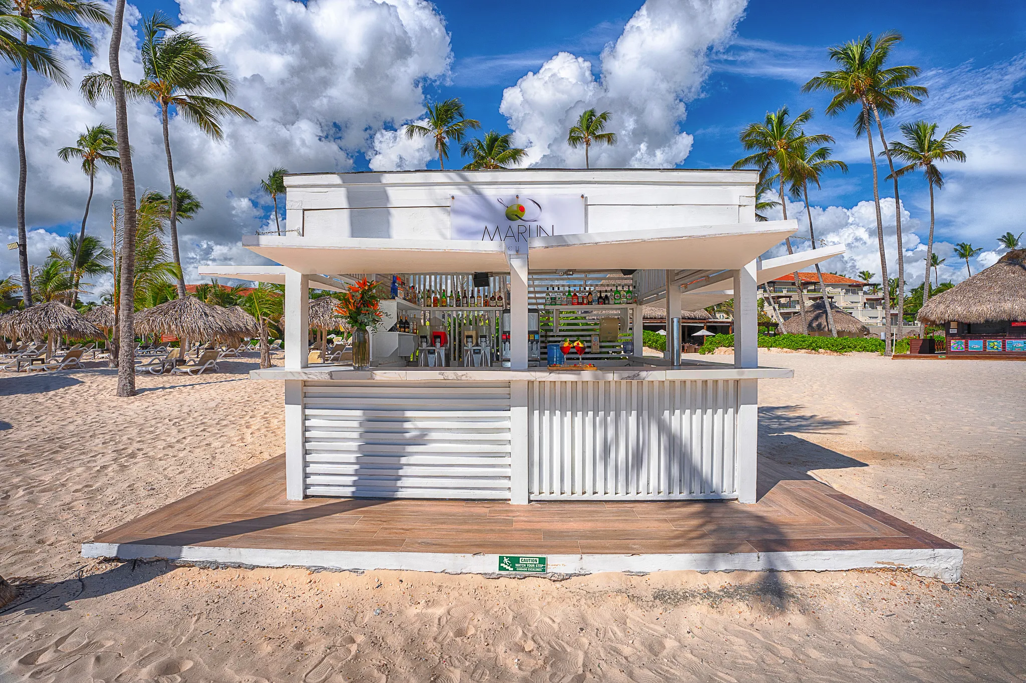 Marlin Beach Bar at Secrets Royal Beach Punta Cana with a white beachfront bar surrounded by palm trees and sandy beach.