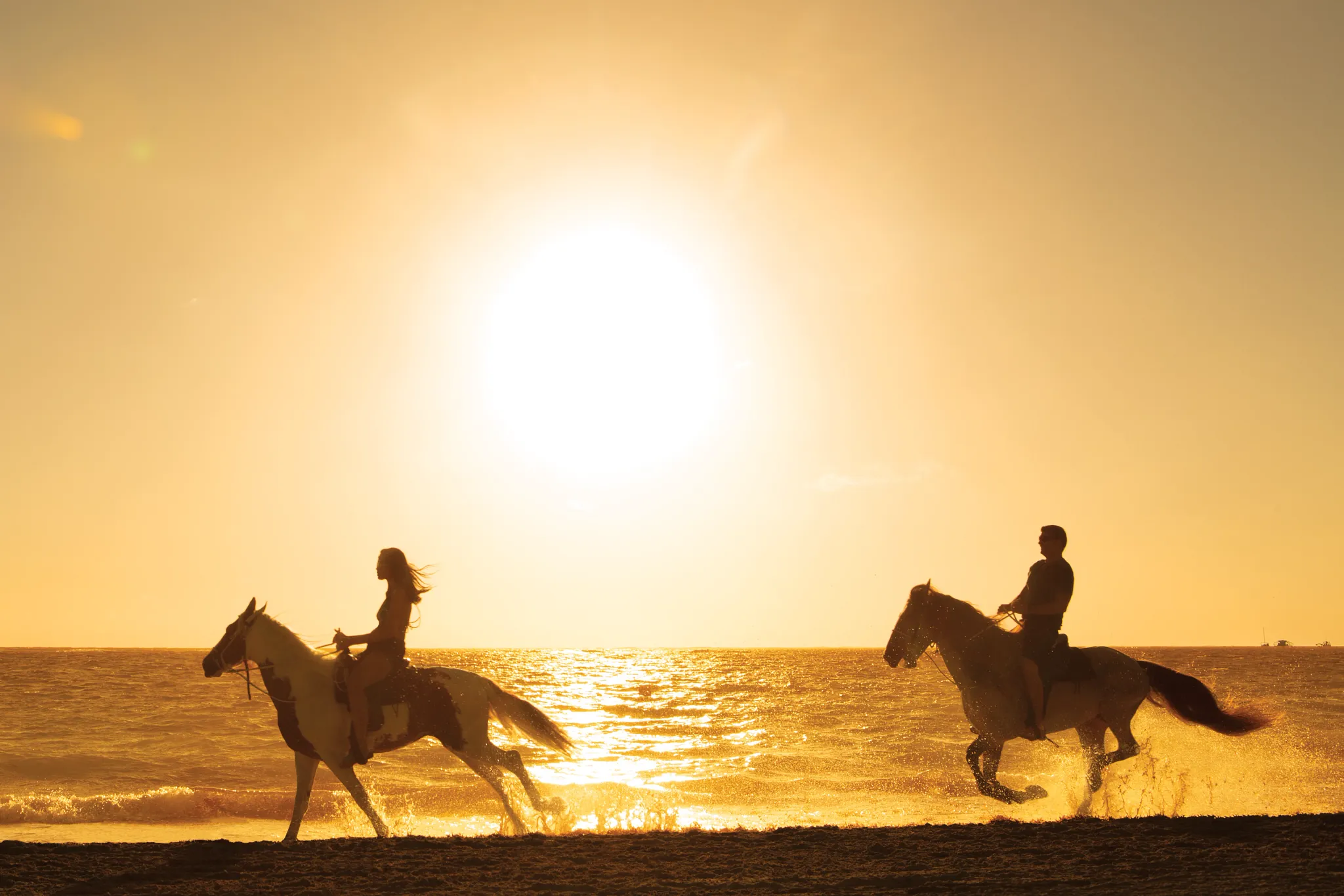 Couple horseback riding along the beach at sunset near Secrets Royal Beach Punta Cana in the Dominican Republic.