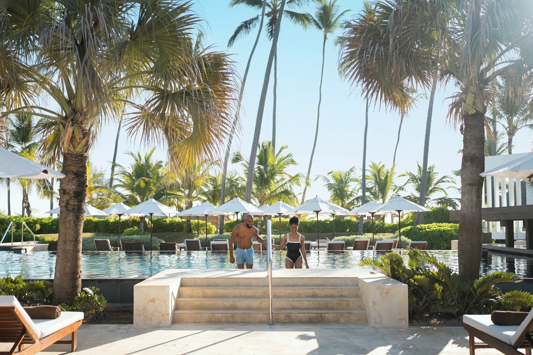 Couple walking out of the infinity pool surrounded by palm trees at Secrets Royal Beach Punta Cana.