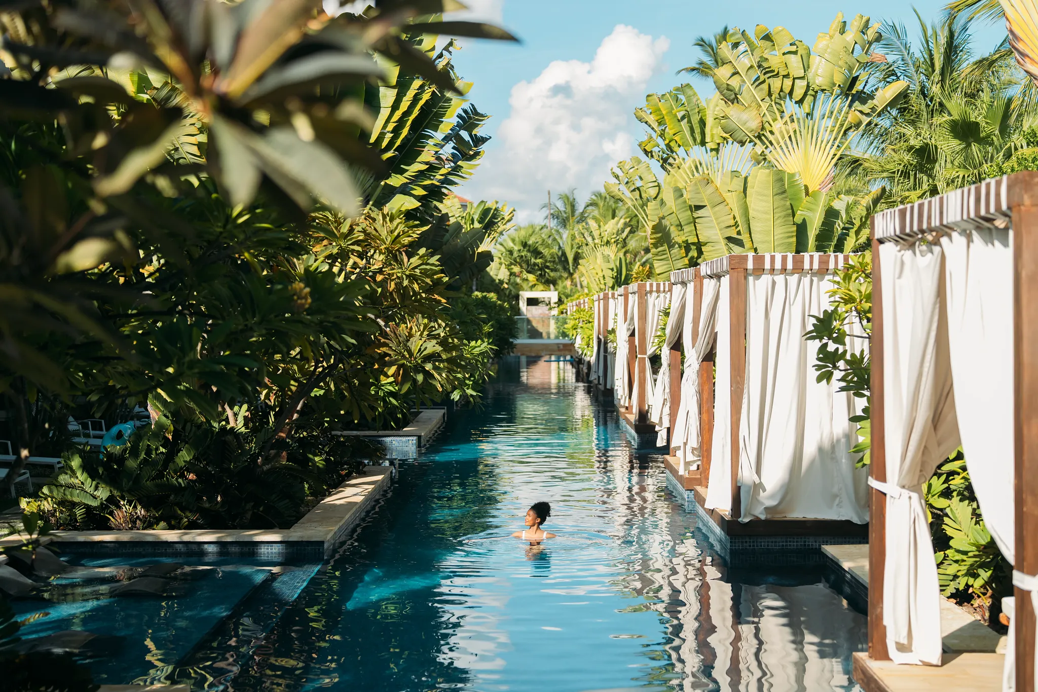 Guest swimming through the long lagoon-style pool lined with cabanas at Secrets Royal Beach Punta Cana.