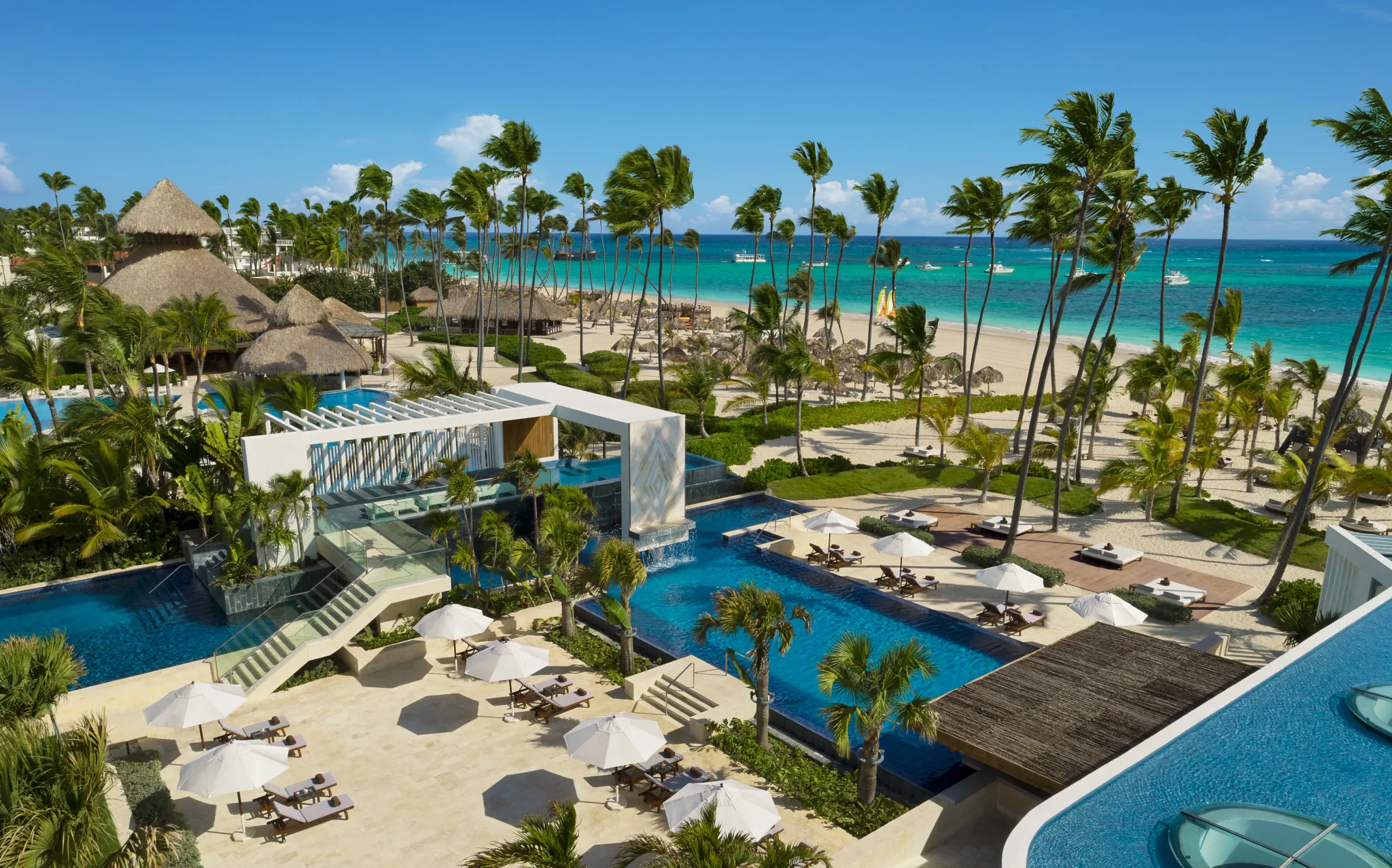 Elevated view of pool decks and beachfront at Secrets Royal Beach Punta Cana with palm trees and sun loungers.