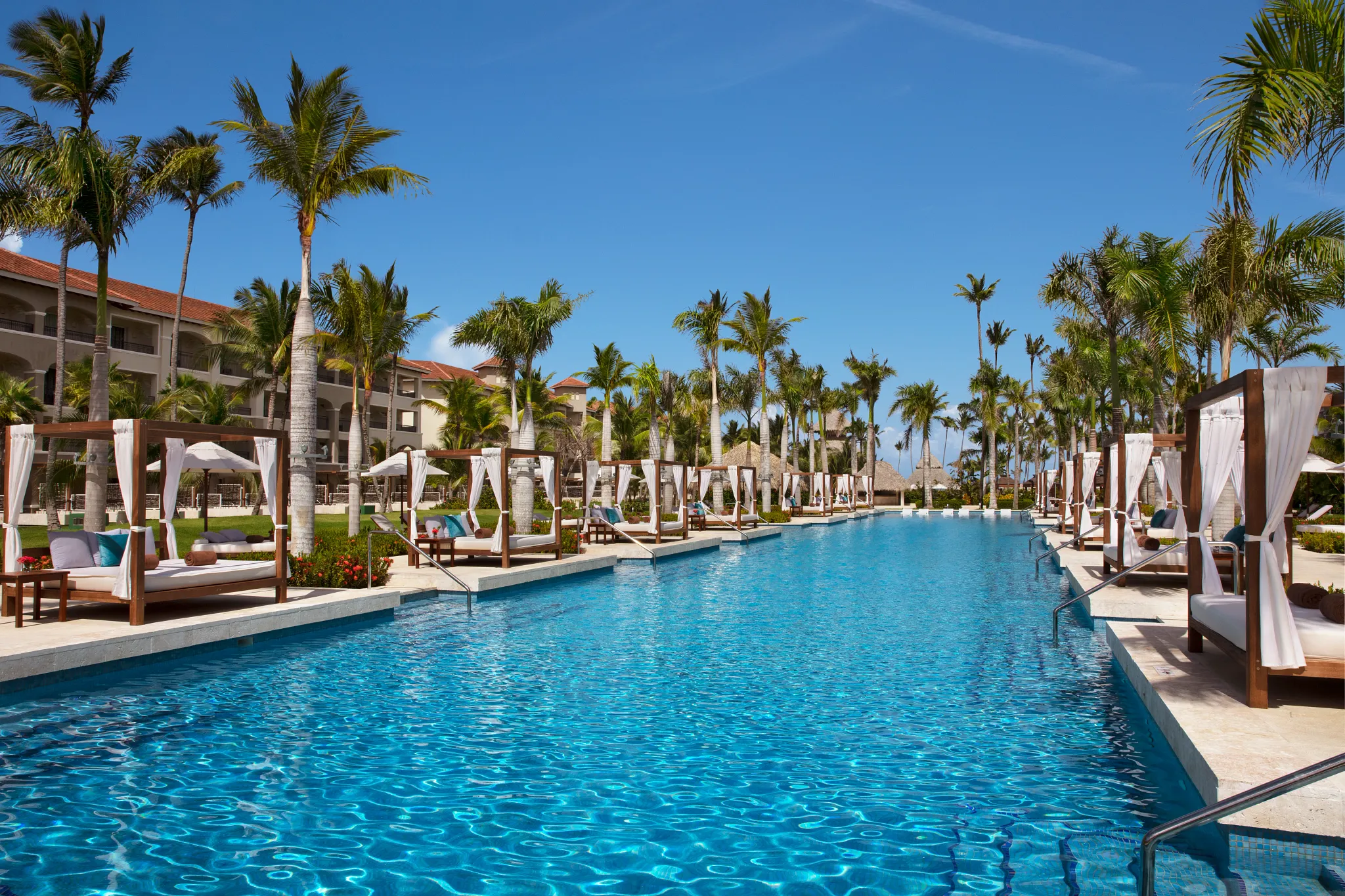 Large lagoon-style relaxation pool with palm trees and cabanas at Secrets Royal Beach Punta Cana.