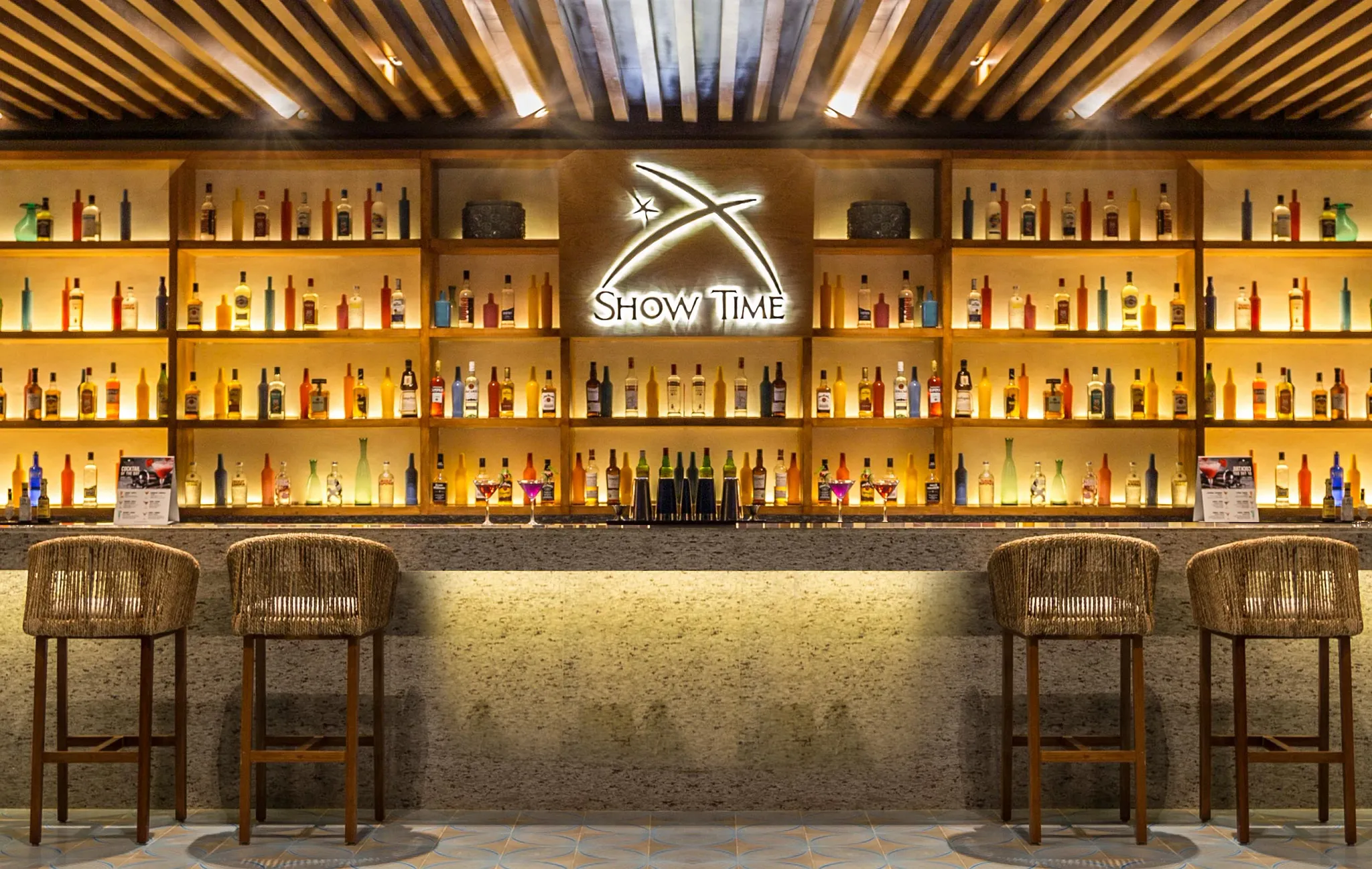 Show Time Sports Bar at Secrets Royal Beach Punta Cana featuring illuminated shelves of spirits and a stylish theater bar setting.
